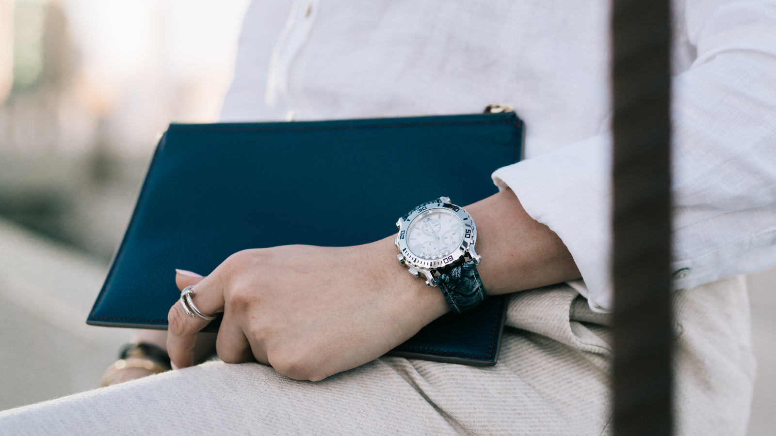 BARWA custom-made alligator watch strap in blue on woman's wrist. Woman is holding BARWA Bannah Clutch in Blue Textured Goatskin.